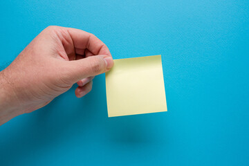 Hand holding blank yellow post-it on blue background