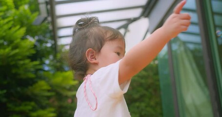 A young Asian child girl enjoying a sunny day outside surrounded by floating soap bubbles in Garden lush greenery in background, capturing the innocence and joy of childhood in natural light.