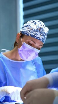 Concentrated female surgeon working at surgery on thyroid. Professional medic at work in modern surgery room. Vertical video.