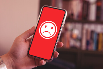 Holding smartphone screen showing bad feeling emoticon on screen at restaurant. concept of...