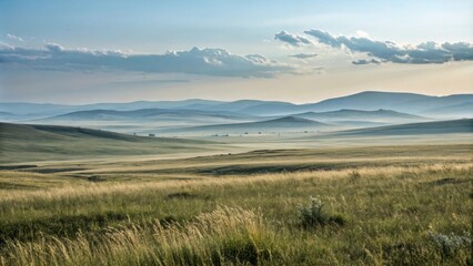 Obraz premium A rolling green field stretches towards distant hazy hills under a sky with scattered clouds.