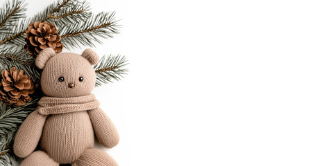 Knitted teddy bear in the color of mocha mousse on the background of fir branches with cones. White background, empty space for text.