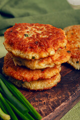 Crispy potato pancakes Latkes, stacked on a wooden board next to fresh green onions, natural light, homemade, no people,