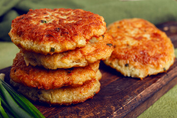 Crispy potato pancakes Latkes, stacked on a wooden board next to fresh green onions, natural light, homemade, no people,
