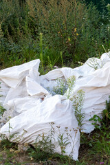 There is a large pile of white bags that are laying on the ground in the grass