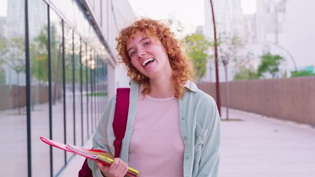 Cheerful red-haired student holding a red folder in a bright outdoor setting