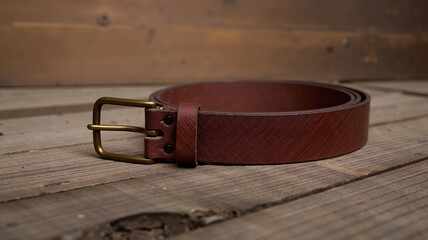 Brown leather belt with brass buckle on wooden surface