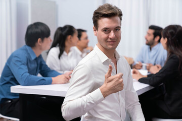 Confidence and happy smiling businessman portrait with background of his colleague and business team working in office. Office worker teamwork and positive workplace concept. Prudent