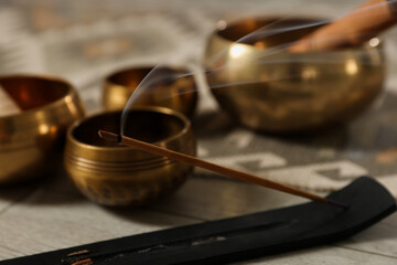 Incense stick smoldering in holder and tibetan singing bowls on floor, closeup