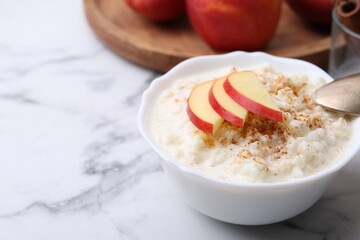 Delicious rice pudding with cinnamon and apple on white marble table, closeup. Space for text