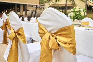 Elegant wedding reception decor with white chairs and golden sashes in outdoor venue.