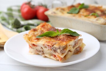 Piece of delicious cooked lasagna with basil on white table, closeup