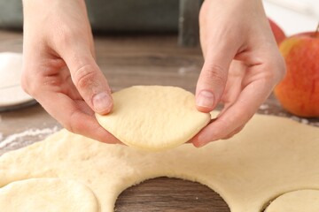 Woman making pirozhki (stuffed pastry pies) at wooden table, closeup