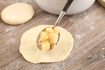 Making pirozhki (stuffed pastry pies). Putting apples onto piece of dough at wooden table, closeup