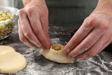 Woman making pirozhki (stuffed pastry pies) with eggs and dill at gray table indoors, closeup