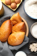 Delicious pirozhki (stuffed pastry pies) and ingredients on grey table, flat lay