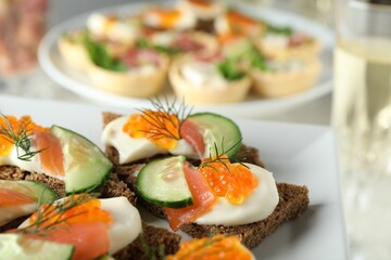 Tasty canapes with salmon and cucumber on plate, closeup