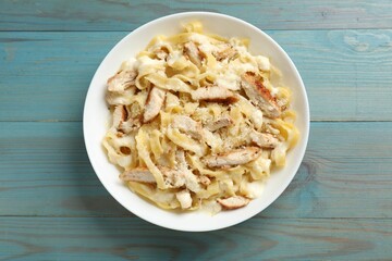 Tasty Alfredo pasta with chicken on light blue wooden table, top view