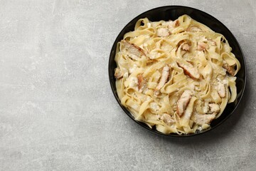 Tasty Alfredo pasta with chicken on light grey table, top view. Space for text