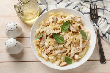 Tasty Alfredo pasta with chicken served on light wooden table, flat lay