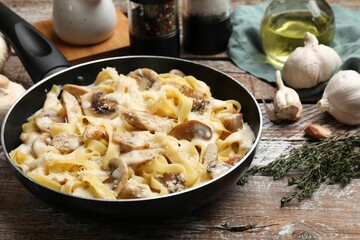 Tasty Alfredo pasta with chicken and mushrooms in frying pan on wooden table, closeup
