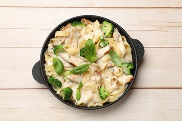 Delicious pasta Alfredo with chicken, cheese, creamy sauce, broccoli and basil on wooden table, top view