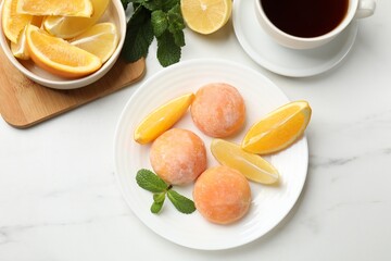 Plate with tasty mochi, cut orange, lemon and mint on white marble table, flat lay