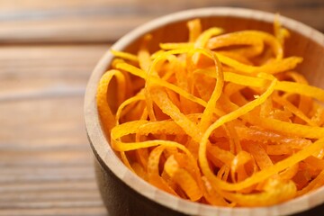 Fresh orange zest in bowl on wooden table, closeup