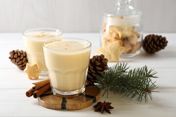 Tasty Christmas cocktail (eggnog) in glasses, pine cones and spices on white wooden table, closeup