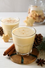 Tasty Christmas cocktail (eggnog) in glasses, pine cones and spices on white wooden table, closeup