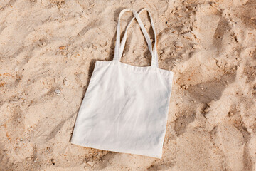White cotton or mesh bag on beach sand background. Zero waste, no plastic, eco friendly shopping, recycling concept. Blank mockup shopper with place for artwork or text. Flat lay, copy space