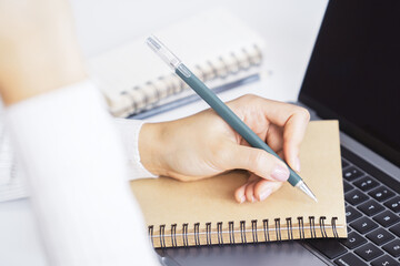 A woman's hand inscribing in a notepad on a modern laptop, captured closely, with a vague background