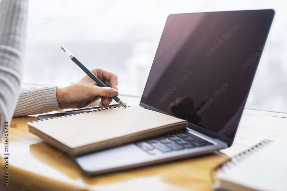 Poster the image highlights a woman's hand writing in a notepad on a laptop, with a faintly blurred surroun