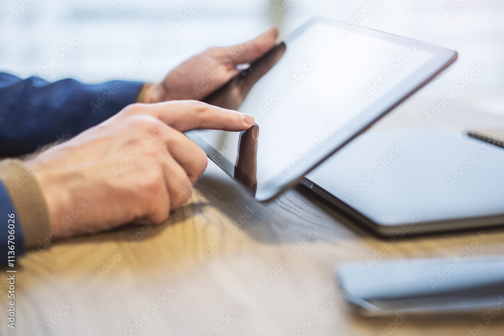 Poster man's finger touching a sleek digital tablet screen placed on a desk, within the softly lit blur of 
