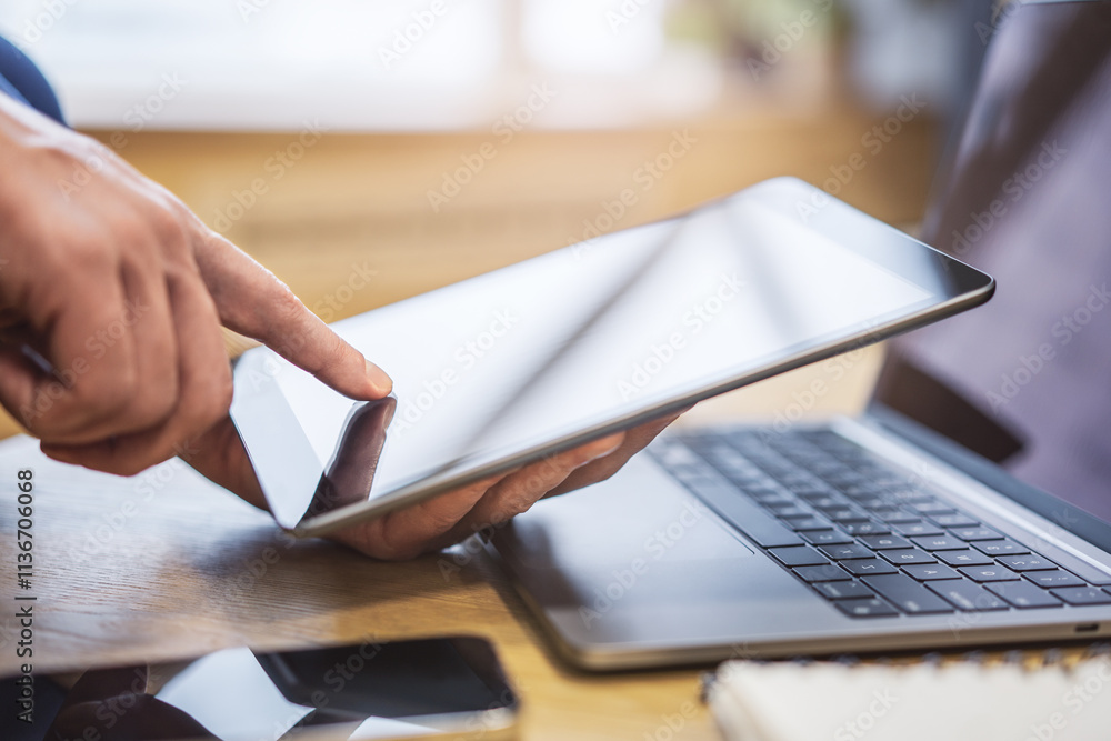 Poster closeup view of a man's finger operating a high-tech tablet on a desk, amidst the blurred backdrop o