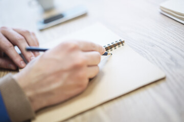 A man's hand is caught in close-up, busily writing in a notepad, while the background is out of...