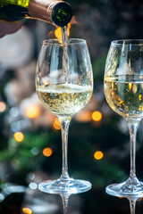 New year or christmas dinner, pouring of glass of dry wite or sweet dessert wine with christmas tree and garland lights on background