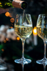New year or christmas dinner, pouring of glass of dry wite or sweet dessert wine with christmas tree and garland lights on background