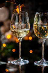 New year or christmas dinner, pouring of glass of dry wite or sweet dessert wine with christmas tree and garland lights on background