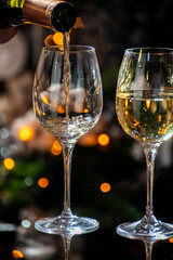 New year or christmas dinner, pouring of glass of dry wite or sweet dessert wine with christmas tree and garland lights on background