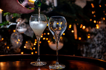 New year or christmas dinner, pouring of glass of brut champagne or cava, prosecco sparkling wine with christmas tree and garland lights on background