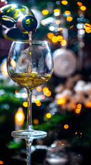 New year or christmas dinner, pouring of glass of dry wite or sweet dessert wine with christmas tree and garland lights on background