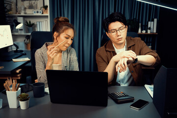 Sales managers waiting email sending back while looking watch with overtime for working report data analysis overworked project job with coworker at over late night time at modern office. Infobahn.