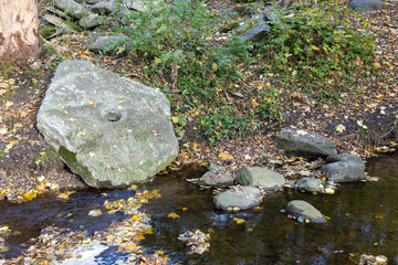 old mill stone laying by a river with autumn color leaves