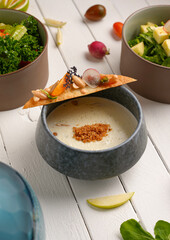 Delicious almond soup with toast, garnished with herbs, tomatoes and almonds, white wooden background