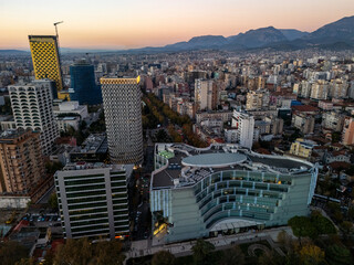 Aerial view of Tirana, Albania, showcasing modern architecture and urban landscape at sunset with mountains in the background.