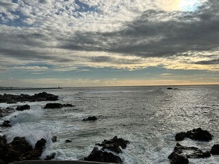 Foz do Douro, Porto, Portugal - 13th December 2024 - Dramatic seascape with historic lighthouse visible on horizon as Atlantic waves crash against rocky coastline under vast winter cloudscape.