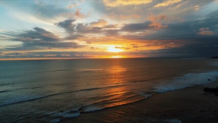 Drone view flying down at sunset over the ocean with waves. Surfers looks like small points from the height of Aerial. Sea and sky are painting with orange and yellow colors. High quality 4k footage