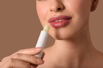 Young woman with lip balm on brown background, closeup