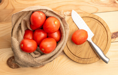 Fresh juicy tomatoes in a jute bag on a wooden table, close-up, top view.